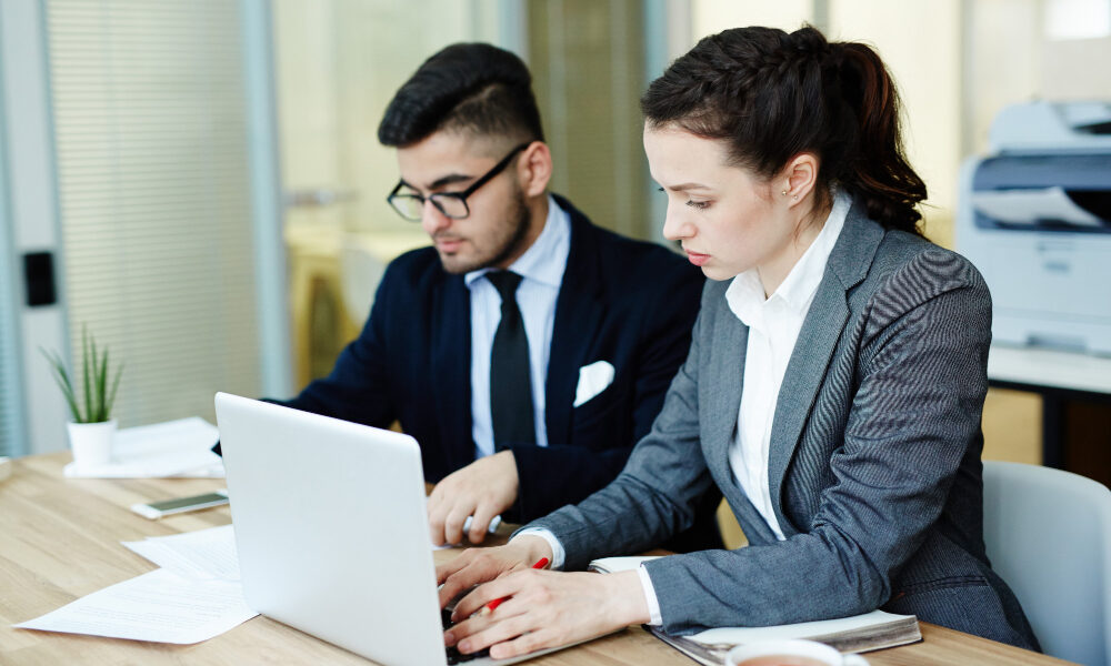 A professional male and female IT team at Tec Nexora, seated at a desk and working collaboratively on a laptop to provide expert technology solutions.